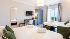 A hotel room with two beds, a desk, a TV, and a large window.
