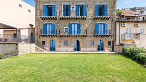 A multi-story stone building with blue shutters, a central courtyard, and a view of the surrounding neighborhood.