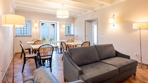 A room with a grey sofa, dining table with chairs, and a ceiling with exposed beams.