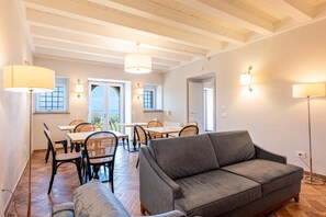 Una habitación con un sofá gris, una mesa de comedor con sillas y un techo con vigas a la vista.