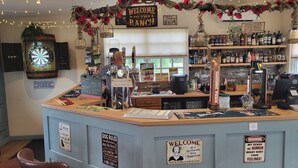 Un bar avec un jeu de fléchettes, des étagères remplies de bouteilles d’alcool et un panneau accueillant les visiteurs au ranch.