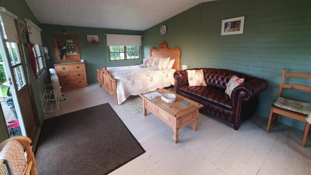 Une pièce comprenant un lit, un canapé en cuir, une commode en bois et une petite table. On peut voir une fenêtre et une porte.