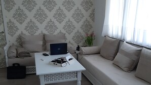 Olohuone, jossa on sohva, sohvapöytä, kannettava tietokone, maljakko kukkineen ja kuviollinen tapetti.
