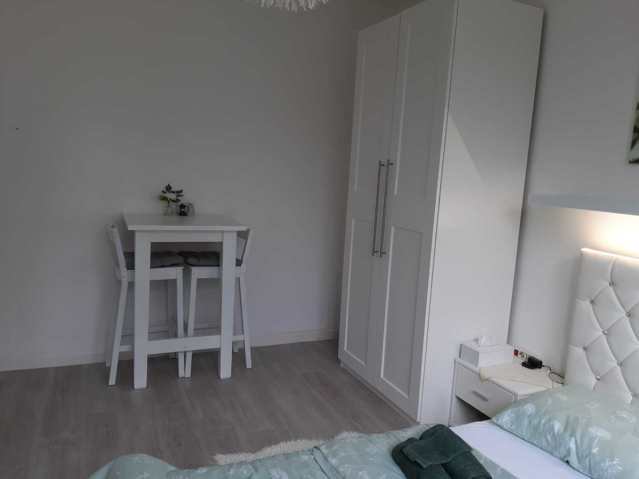 A bedroom with a bed, a bedside table, a wardrobe, a desk, and a chair.