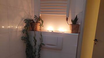 A bathroom with a toilet, a shower area, a sink, and a small window with a plant.