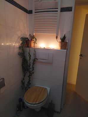 Un baño con inodoro, zona de ducha, lavamanos y una pequeña ventana con una planta.
