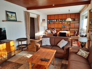 A living room with a brown leather sofa, a wooden coffee table, a bookshelf, and a television.