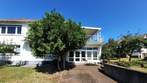 Un edificio bianco con un balcone, un albero di fronte e un vialetto in mattoni.