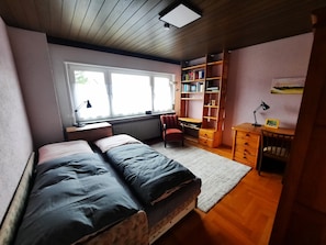 A bedroom with a bed, a desk, a chair, a bookshelf, and a window.