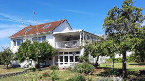 Un edificio a due piani con un balcone, un giardino e un cielo azzurro limpido.