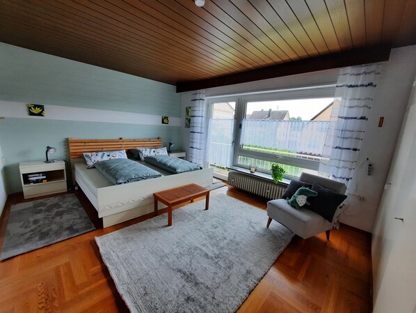 A bedroom with a wooden ceiling, a bed with a headboard, a nightstand, a window with a view, and a radiator.