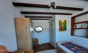 A bedroom with a bed, a wooden wardrobe, a mirror, a door leading to another room, and a painting on the wall.