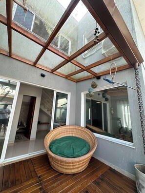 A covered patio with a wicker chair, wooden flooring, and a glass ceiling. - Beautiful two-story house in the Morada da Praia condominium. (Bertioga)