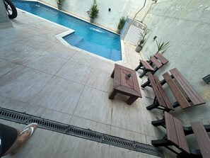 A swimming pool with a tiled deck, surrounded by potted plants and wooden picnic tables. - Beautiful two-story house in the Morada da Praia condominium. (Bertioga)