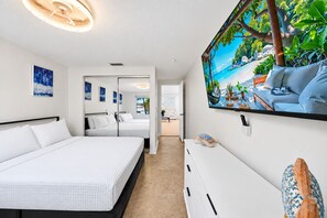 A hotel room with a large bed, a desk, a TV, and a view of a beach through a window. - Private Pool Retreat in Tampa | 5BR/5BA Vacation Home (Tampa)