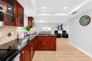 Eine moderne Küche mit Holzausbau, einer schwarzen Arbeitsplatte und einer zentralen Kochinsel. Es gibt einen Essbereich mit zwei schwarzen Stühlen und einem Gemälde an der Wand.