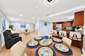 A modern living room with a sofa, chairs, a dining table with placemats, and a kitchen area with cabinets and appliances. - Private Pool Retreat in Tampa | 5BR/5BA Vacation Home (Tampa)