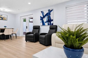 Ein modernes Wohnzimmer mit Essbereich, zwei schwarzen Ledersofas, einem weißen Sofa, einem blauen Blumentopf und abstrakter Kunst an der Wand.