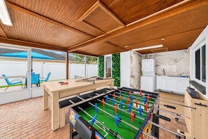 A room with a foosball table, a kitchen area, and a seating area with chairs. - Private Pool Retreat in Tampa | 5BR/5BA Vacation Home (Tampa)