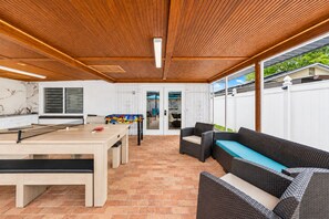 Une terrasse extérieure avec une table de billard, des meubles en osier et une vue sur le jardin.