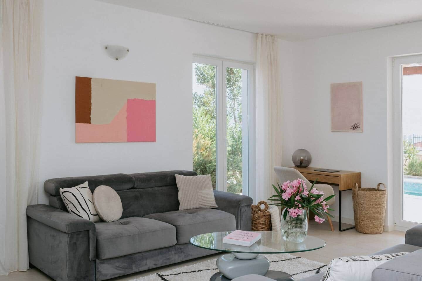 Ein modernes Wohnzimmer mit einem grauen Sofa, einem Glastisch und einem Schreibtisch mit einer Lampe.