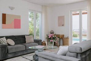Uma sala de estar moderna com um sofá cinzento, uma mesa de centro de vidro e vista para uma piscina.