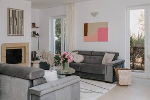 Uma sala de estar moderna com lareira, sofás cinzentos, uma mesa de centro de vidro e uma janela grande com vista.