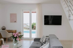 A modern living room with a sofa, a TV, a desk, and a view of a swimming pool. - Villa Oleander: Pool & Rooftop Cinema (Splitska)