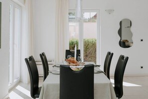A dining area with a table set for four, black chairs, a white tablecloth, and a view of greenery outside. - Villa Oleander: Pool & Rooftop Cinema (Splitska)