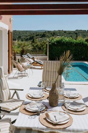 A dining table set for four with a view of a pool and greenery. - Villa Melograno: Pool & Rooftop Cinema (Splitska)