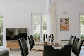 Un coin repas équipé d’un téléviseur, de chaises noires, d’un meuble en bois et d’une table dressée pour quatre personnes.