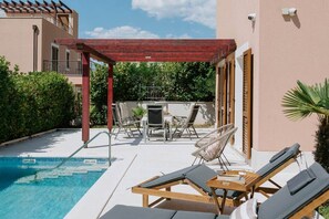 A pool area with lounge chairs, a table, and chairs under a wooden pergola. - Villa Melograno: Pool & Rooftop Cinema (Splitska)