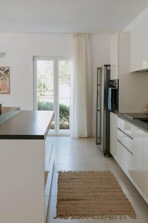 Eine moderne Küche mit einer Schiebeglastür, die auf einen Balkon führt, einem Kühlschrank und einer Arbeitsplatte.