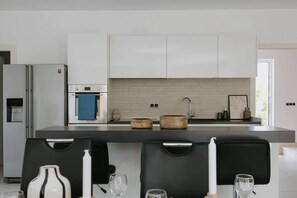 Eine moderne Küche mit weißen Schränken, einem Edelstahl-Kühlschrank, einem Einbauofen und einer großen Kochinsel mit Spüle.