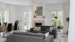 Een moderne woonkamer met een open haard, grijze banken en een eethoek met een tafel en stoelen.