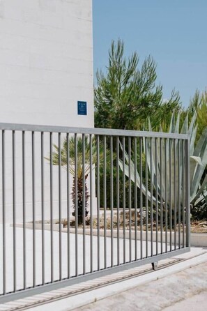 A gated entrance with a metal fence, a white building, and some greenery in the background. - Villa Aurelia: Pool & Rooftop Cinema (Splitska)