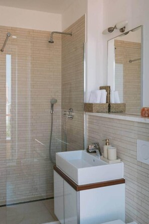 A modern bathroom with a glass shower enclosure, a white sink with a wooden base, and a mirror with a towel rack above it. - Villa Aurelia: Pool & Rooftop Cinema (Splitska)