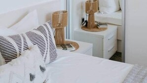 Een slaapkamer met een bed, nachtkastje, lamp en een spiegel.