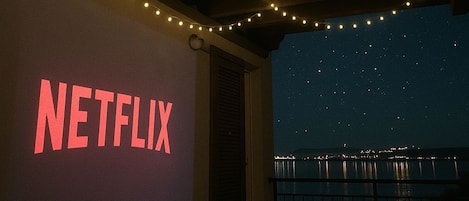 A covered outdoor area with string lights, a balcony with a railing, and a large illuminated sign reading 'NETFLIX'.
