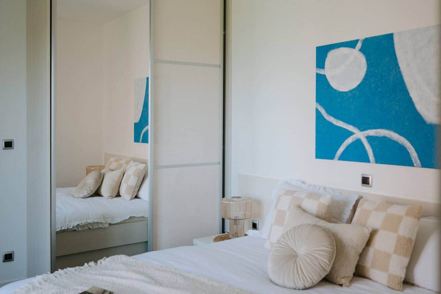 Une chambre moderne avec un grand lit, une table de chevet, une lampe et un miroir.