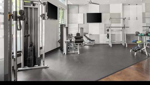 Ein modernes Fitnessstudio mit unterschiedlichen Trainingsgeräten, einem Deckenventilator und einem großen Fenster, das für natürliches Licht sorgt.