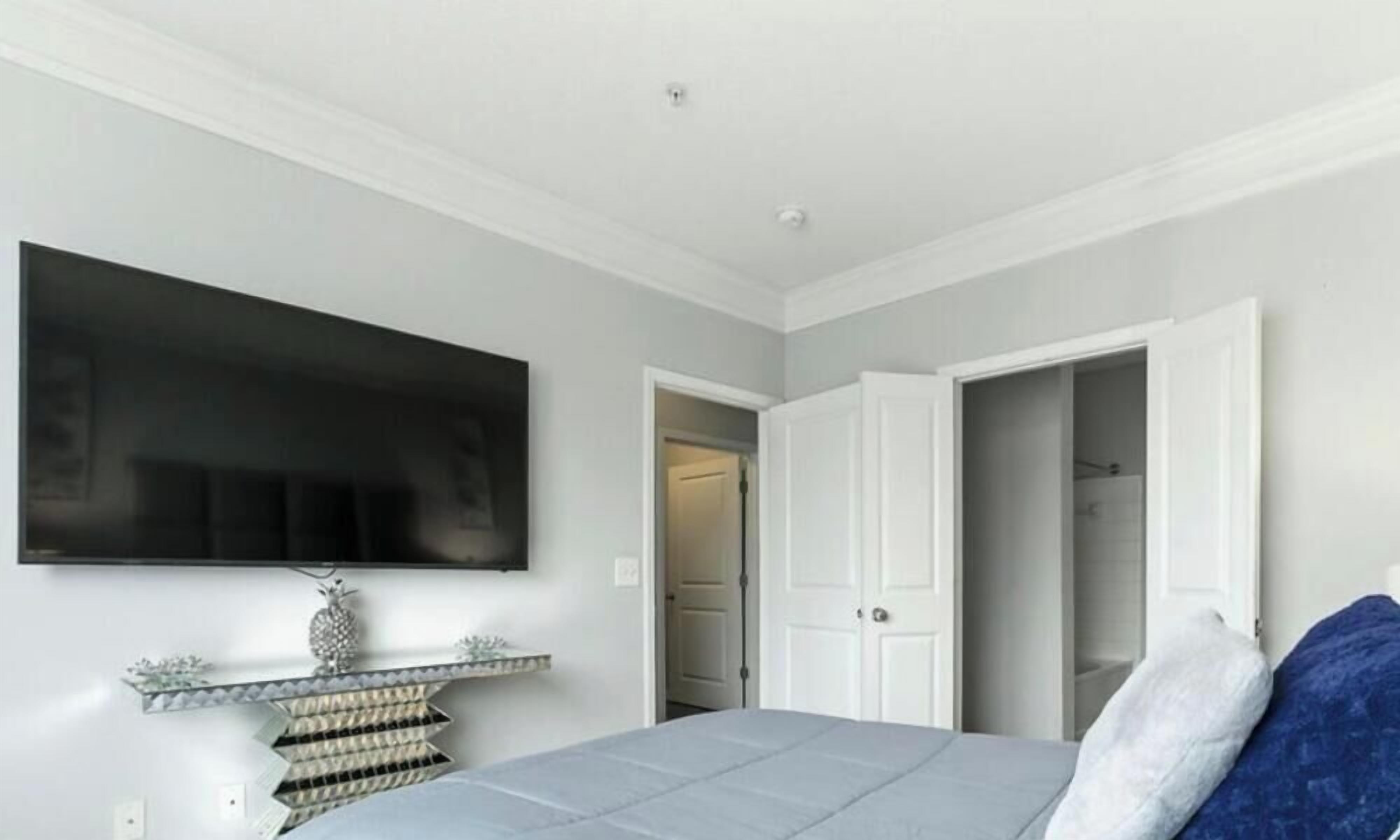 Una camera da letto con un letto, una TV montata a parete, una porta che dà su un bagno e un piccolo ripiano con oggetti decorativi.