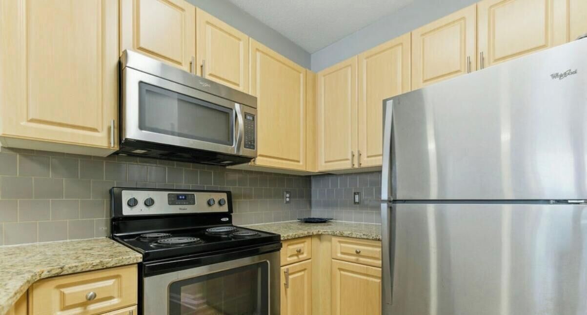 Una cocina con armarios de madera clara, un microondas de acero inoxidable, una estufa y un refrigerador.