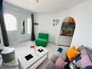 Ein modernes Wohnzimmer mit einer Couch, einem grünen Sessel, einem weißen Couchtisch und einem durch einen Bogen sichtbaren Küchenbereich.