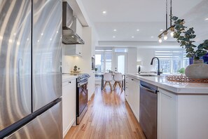 A modern kitchen with stainless steel appliances, wooden flooring, and a view to the dining area.