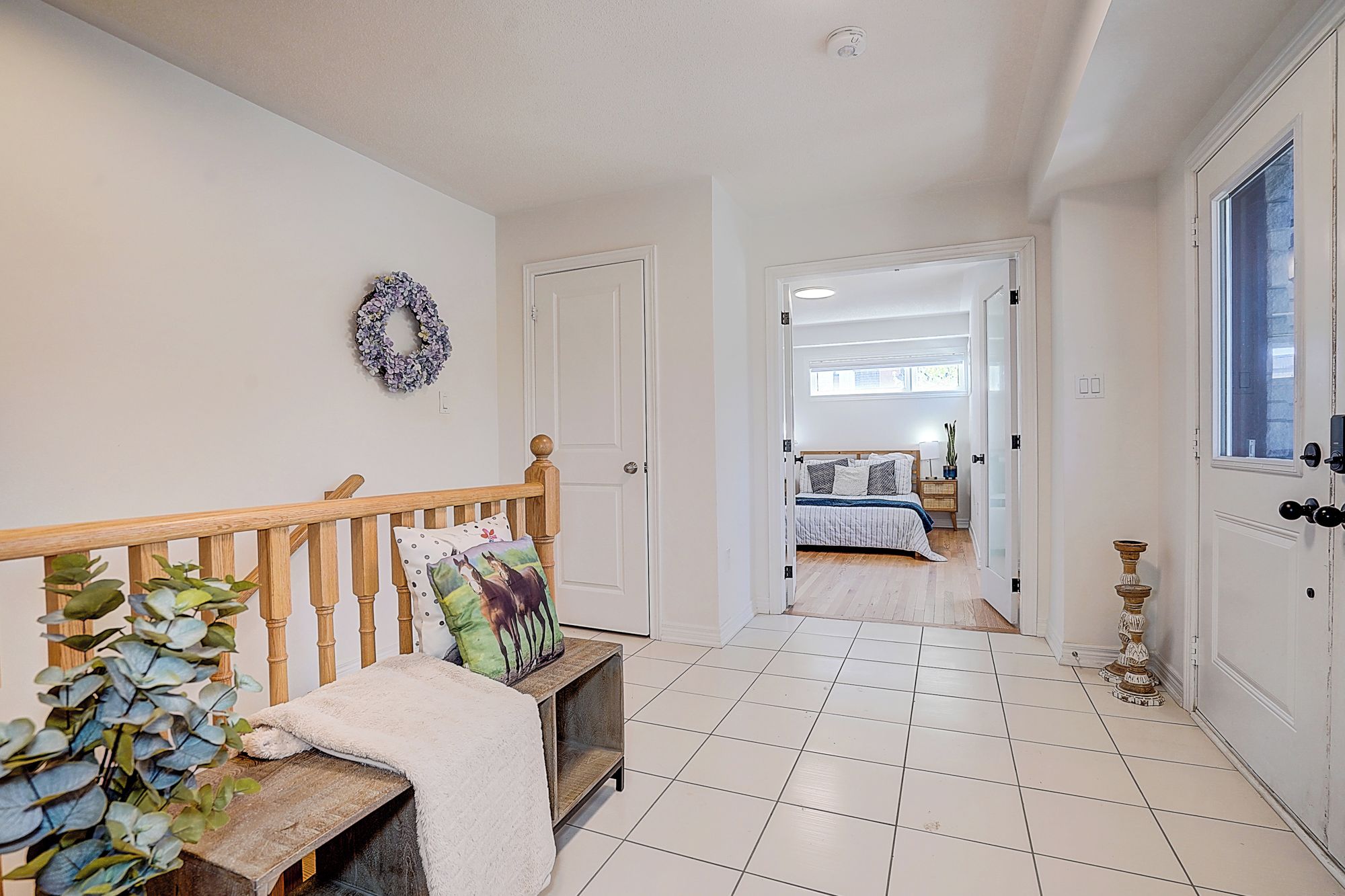 A hallway with a wooden bench, a plant, and a door leading to a bedroom with a bed and a nightstand.