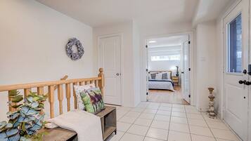 A hallway with a wooden bench, a plant, and a door leading to a bedroom with a bed and a nightstand.