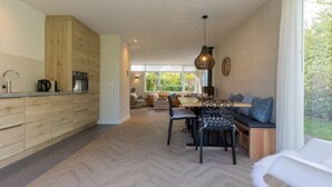 A modern kitchen with wooden cabinets, a dining area with a herringbone floor, and a seating area with a view of greenery. - GroenparkHuis by Interhome (Oostkapelle)