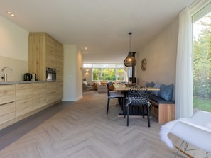 Eine moderne Küche mit Holzausstattung, ein Essbereich mit Fischgrätparkett und eine Sitzecke mit Blick ins Grüne.