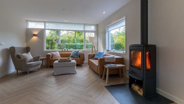 A modern living room with a fireplace, large windows, and a herringbone wood floor. - GroenparkHuis by Interhome (Oostkapelle)